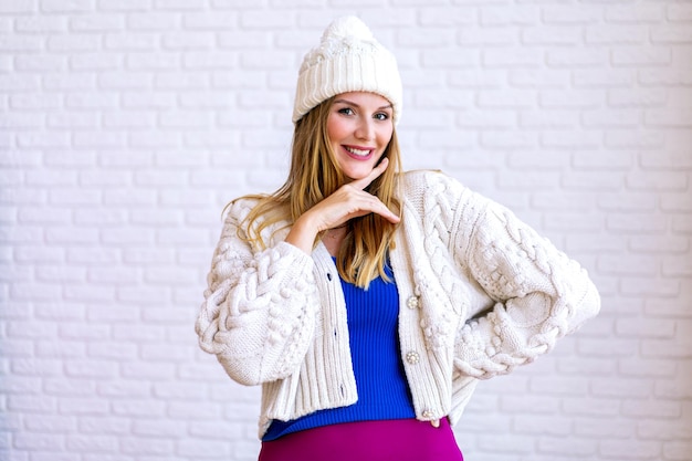 Indoor cute lifestyle portrait of pretty woman wearing warm knitted cardigan and hat, winter holiday Christmas time.