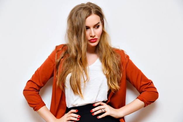 Indoor fashion portrait of pretty blonde woman with amazing fluffy blonde hairs, natural make up, business smart casual look, white wall, flash.