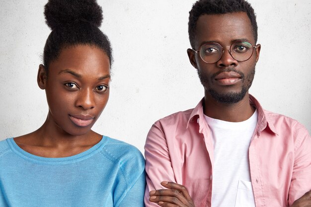 Indoor horizontal shot of confident attractive African American male and female looks with serious expression at camera, meet together to discuss future plans