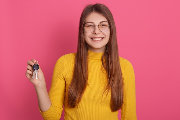 Indoor  image of adorable magnificent young female holding keys, smiling sincerely, 