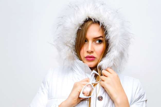 Indoor lifestyle fashion portrait of young blonde woman wearing white winter parka.