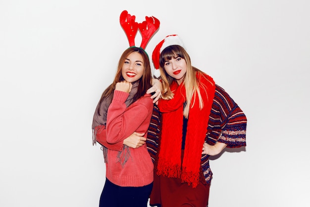 Indoor lifestyle portrait of two best friends.Holiday makeup and cute winter cozy outfit , white wall. Wearing masquerade hats.