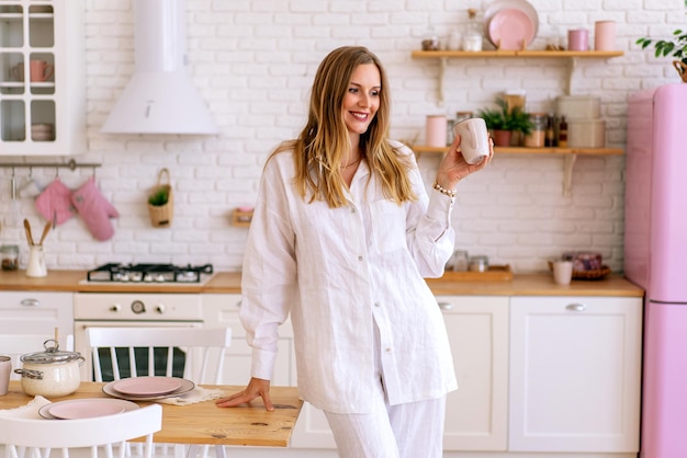 Indoor lifestyle portrait woman wearing white linen suit prepare food in her kitchen, perfect housewife , enjoy her time at home.