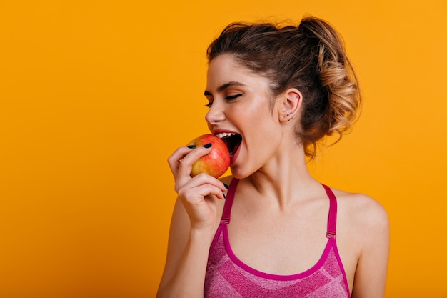 Indoor photo of blissful woman eating apple