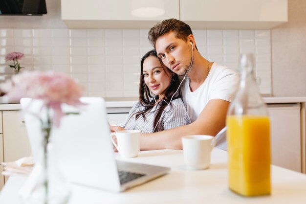 Indoor photo of loving couple using laptop, while chilling in kitchen