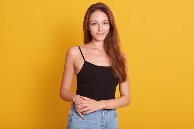 Indoor photo of vivacious woman wearing jeans and black t-shirt posing on camera with pleasant smile and. Copy space for advertisment.