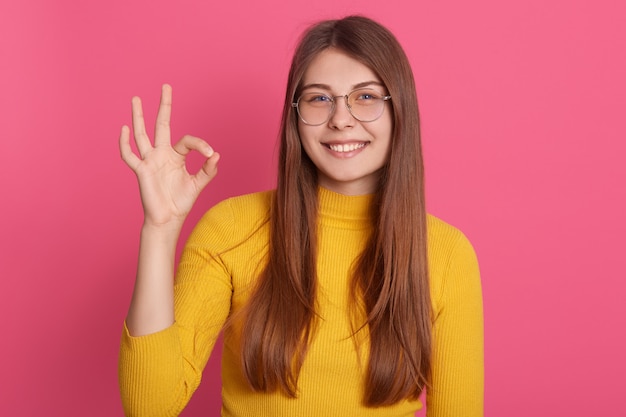 Indoor picture of sincere cheerful young model making gesture, showing sign okay, having gap in teeth