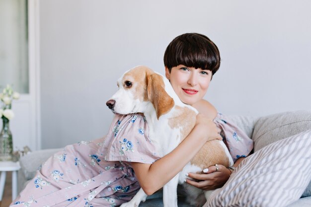 Indoor portrait of attractive girl with short hairstyle embracing big puppy with black eyes