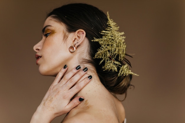 Free photo indoor portrait of beautiful girl with plant in black hair. stylish blithesome lady posing on brown wall.