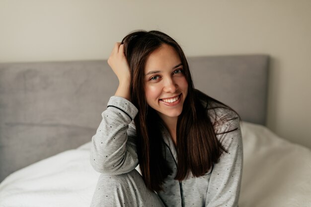 Indoor portrait of charming pretty woman with dark hair smiling while wake up in the morning at home.