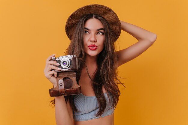 Indoor portrait of enchanting long-haired girl holding camera and looking away