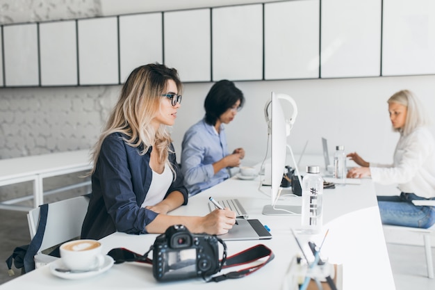 Ritratto dell'interno delle ragazze europee che lavorano al progetto con il collega asiatico in ufficio e parlando