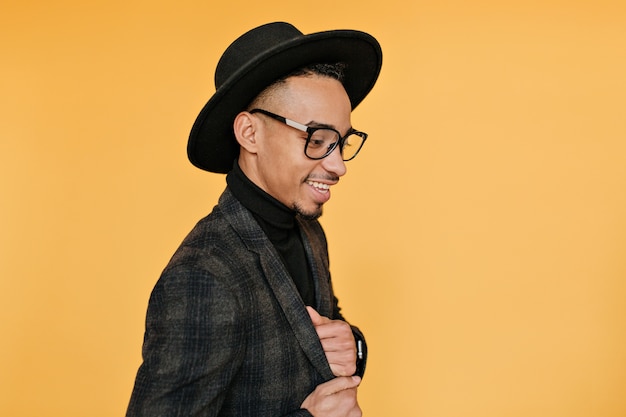 Indoor portrait of good-looking mulatto guy spending time with bright interior. photo of fashionable black male model looking down during photoshoot.