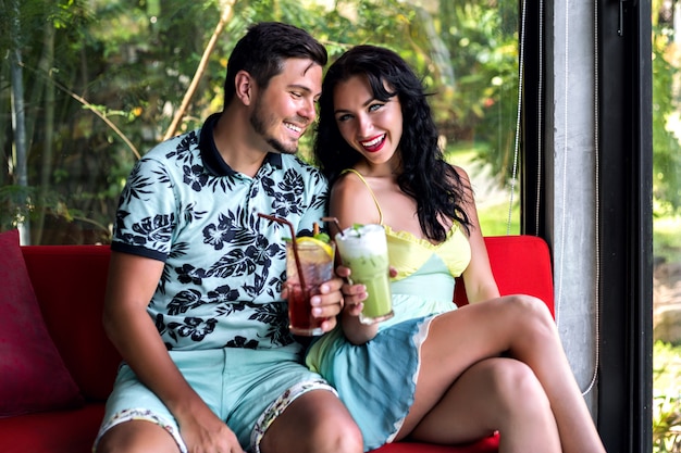 Indoor portrait of happy stylish couple enjoying their romantic date, drinking tasty sweet alcohol drinks, elegant clothes, fancy restaurant.