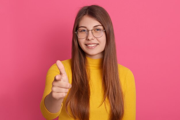 Indoor portrait of pleasant cheerful young lady posing isolated over pink wall in studio, smiling sincerely, making gesture, being in high spirits, spending time alone. Emotions concept.