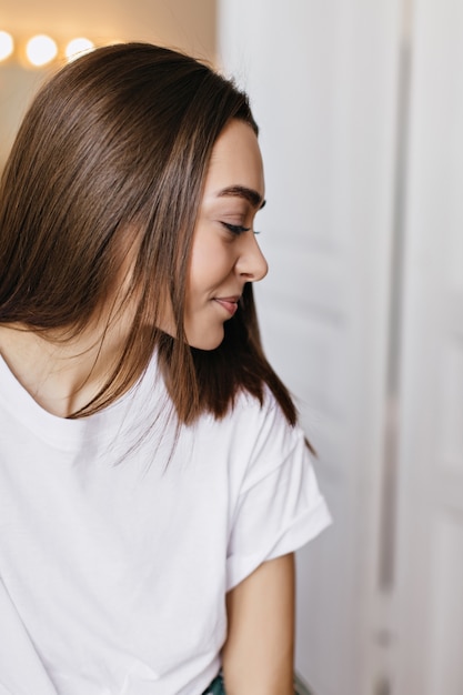 Free photo indoor portrait of pleasant girl with brown shiny hair. shy smiling woman posing at home in weekend.