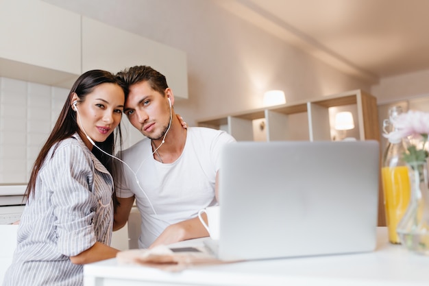 Indoor portrait of pleased married couple spending weekend morning together and using laptop