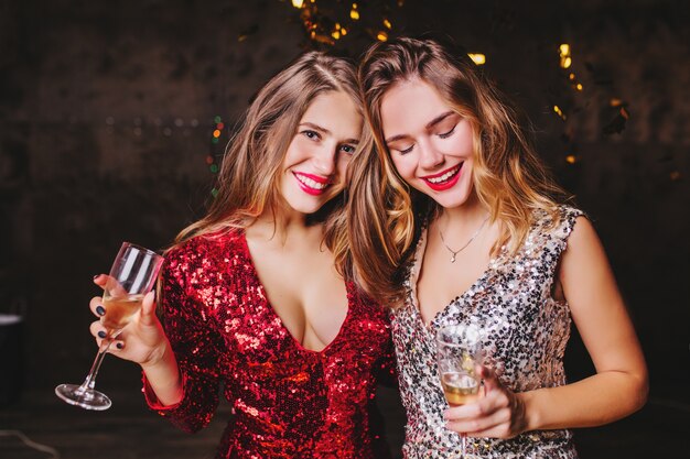 Indoor portrait of pleased woman in trendy sparkle attire enjoying christmas party with best friend