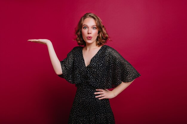 Indoor portrait of pleased young woman in beautiful black dress posing at home