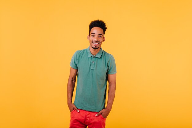 Indoor portrait of smiling black man standing with hands in pockets. blithesome african guy isolated.