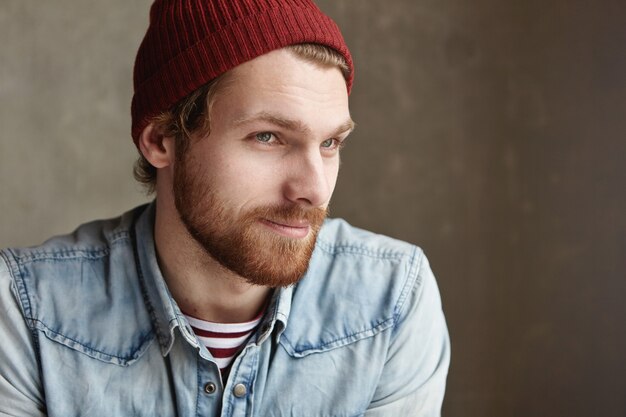 Indoor portrait of stylish good-looking young bearded hipster in trendy clothes with joyful smile