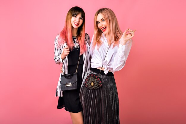 Indoor  portrait of two happy best friends sisters women, wearing trendy black and white clothes and pink hairs, glamorous evening feminine outfits, party mood