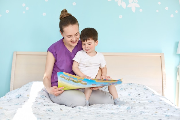 Indoor shot of affectionate woman and small boy read interesting story from book