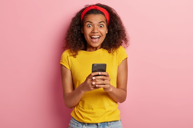 Indoor shot of amused teenage girl with curly hair posing in yellow tshirt