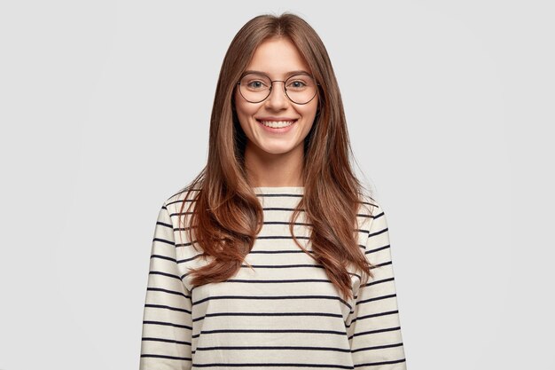 Indoor shot of attractive young woman with glasses posing against the white wall