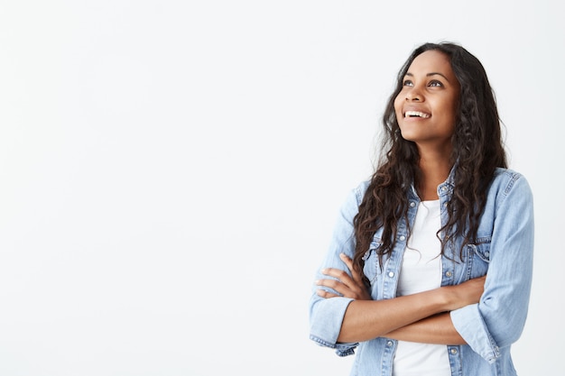 Free photo indoor shot of beautiful happy afro-american female employee standing isolated on white smiling cheerfully, keeping her arms folded, relaxing indoors after work.
