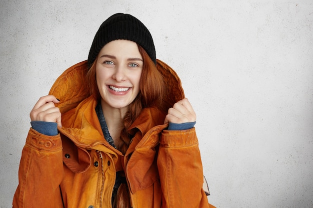 Indoor shot of beautiful redhead Caucasian girl in black hat, smiling happily