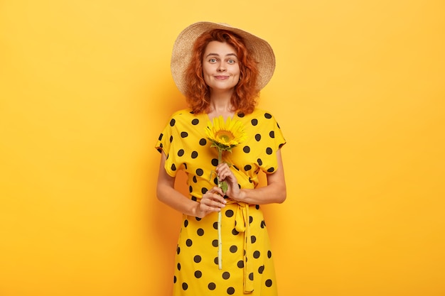 Free photo indoor shot of beautiful smiling red haired woman holds sunflower