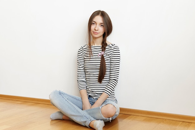 Free photo indoor shot of beautiful teenage girl with messy hair in loose braid wearing casual striped top