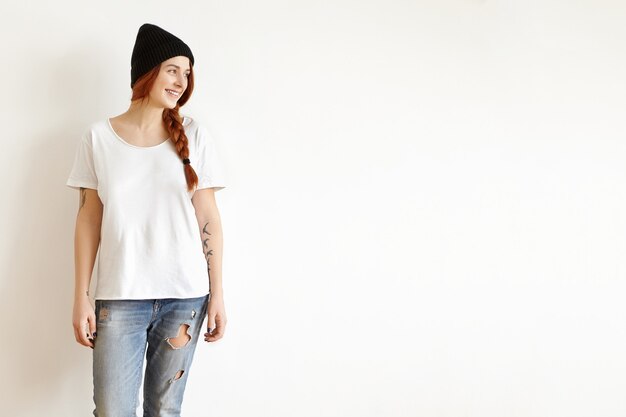 Indoor shot of beautiful young woman in stylish clothing posing isolated against white studio wall