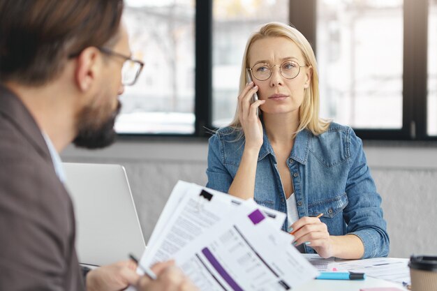 Indoor shot of blonde female having business conversation with colleague