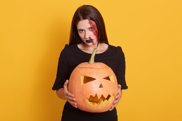 Крытый выстрел брюнетка женщины в Хэллоуин макияж, держа тыкву на желтом