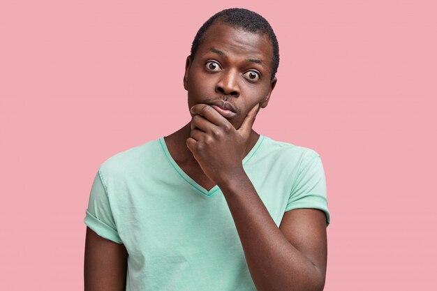 バグのある目をしたハンサムなアフリカ系アメリカ人男性の屋内ショットは、あごを保持し、注意深い慎重な表情で情報を聞きます