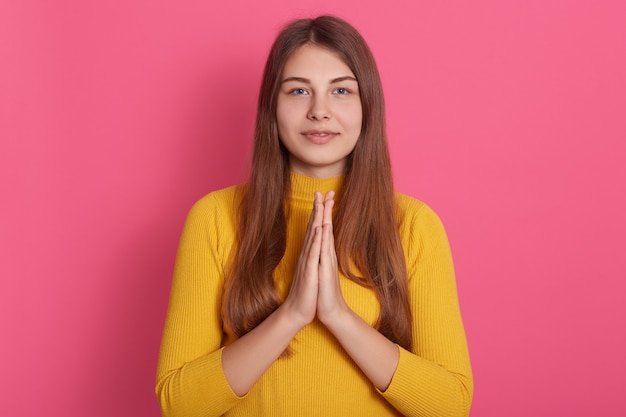 Indoor shot of calm Caucasian lady standing with palms together in front of her chest