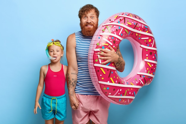 Крытый снимок восхищенных рыжих отца и дочери, позирующих в костюмах для бассейна
