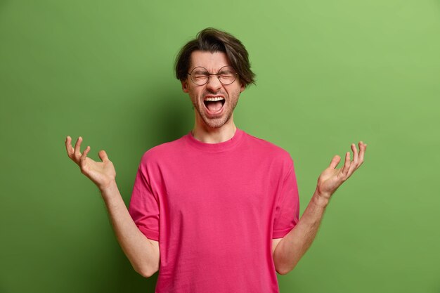 Indoor shot of desperate angry man exclaims loudly raises hands with frustrated expression has fault or problem in life