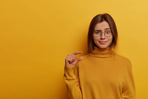 Indoor shot of displeased cute woman makes little size gesture, shapes something very small