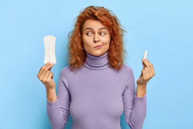 Indoor shot of doubtful female model hesitates between two hygiene products