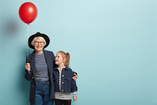 Indoor shot of fashionable senior woman embraces little child, enjoy spending time together