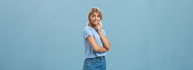 Indoor shot of feminine romantic and timid goodlooking european female with fair hair holding finger