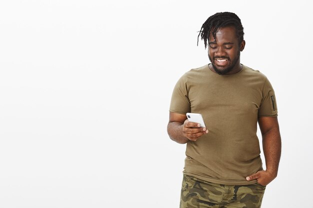 Indoor shot of good-looking happy guy in a brown t-shirt posing against the white wall with his phone