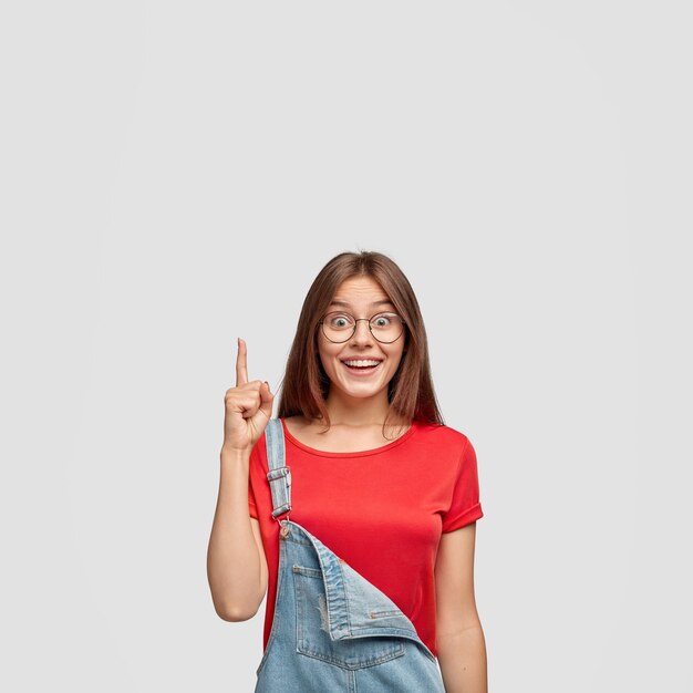 Indoor shot of good looking satisfied brunette woman has pleased facial expression, gets brilliant idea in mind