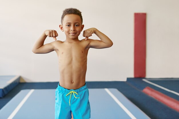 運動体とフィットネスセンターでの強い腕のトレーニングを持つハンサムなアフリカ系アメリカ人の少年の屋内ショット