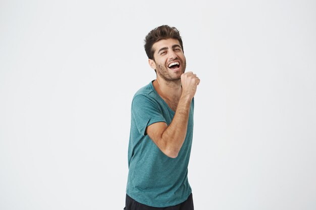 Indoor shot of handsome excited lucky young hipster in excitement, cheering, because of passing all exams at college. positive emotions and feelings