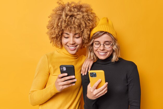 幸せな美しい女性の屋内ショットは、モバイルオファーを楽しんでいます新しいアプリケーションやウェブサイトを閲覧する現代の技術に夢中になっているセルラーチャットを鮮やかな黄色の背景で分離してオンラインで保持します