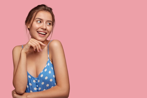 Indoor shot of happy young Caucasian woman keeps hand under chin